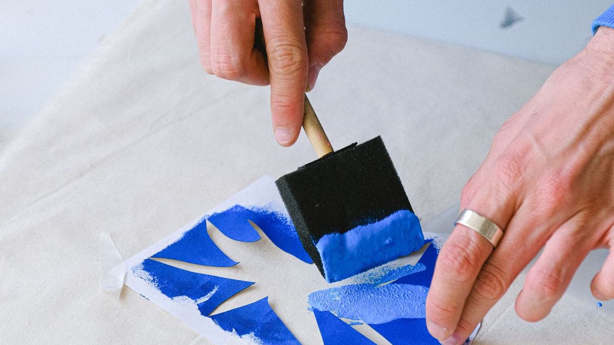 Pessoa aplicando tinta azul com pincel sobre um stencil