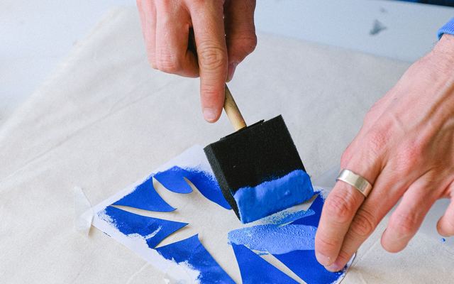 Pessoa aplicando tinta azul com pincel sobre um stencil