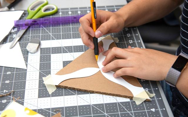 Pessoa recortando papelão e papel sobre uma base de corte