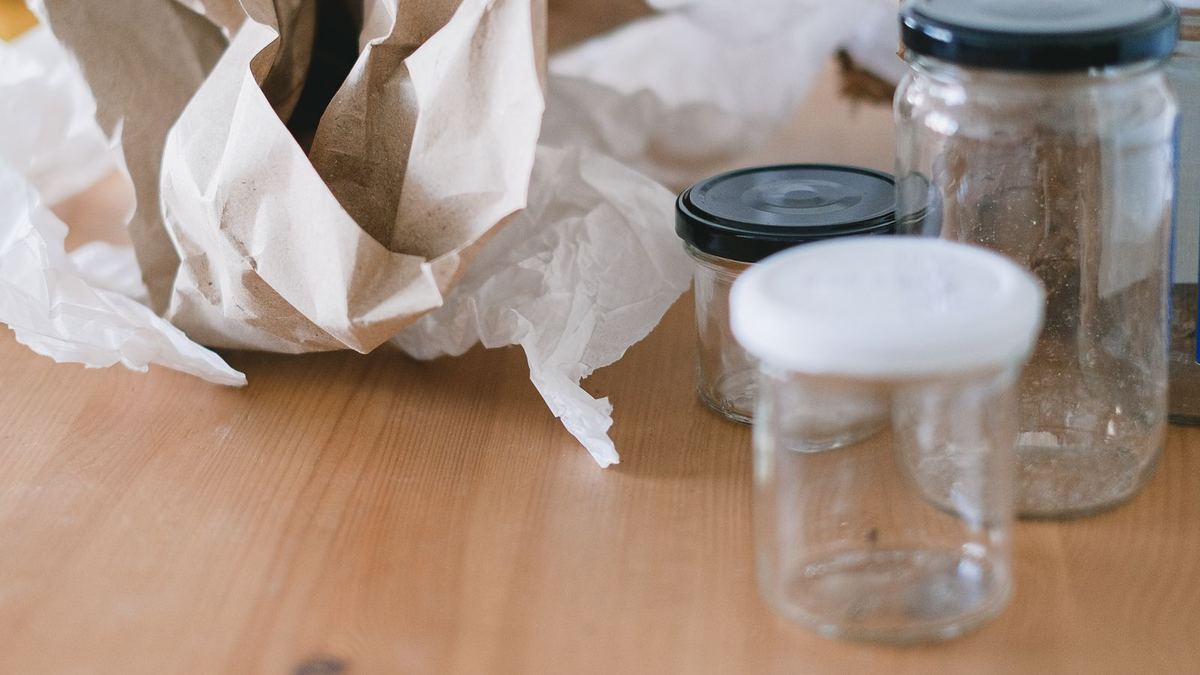 Potes de vidro vazios com tampas ao lado de papel amassado, separados para reaproveitar