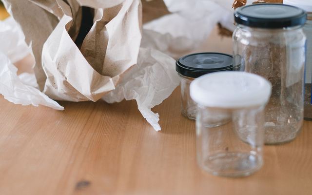 Potes de vidro vazios com tampas ao lado de papel amassado, separados para reaproveitar