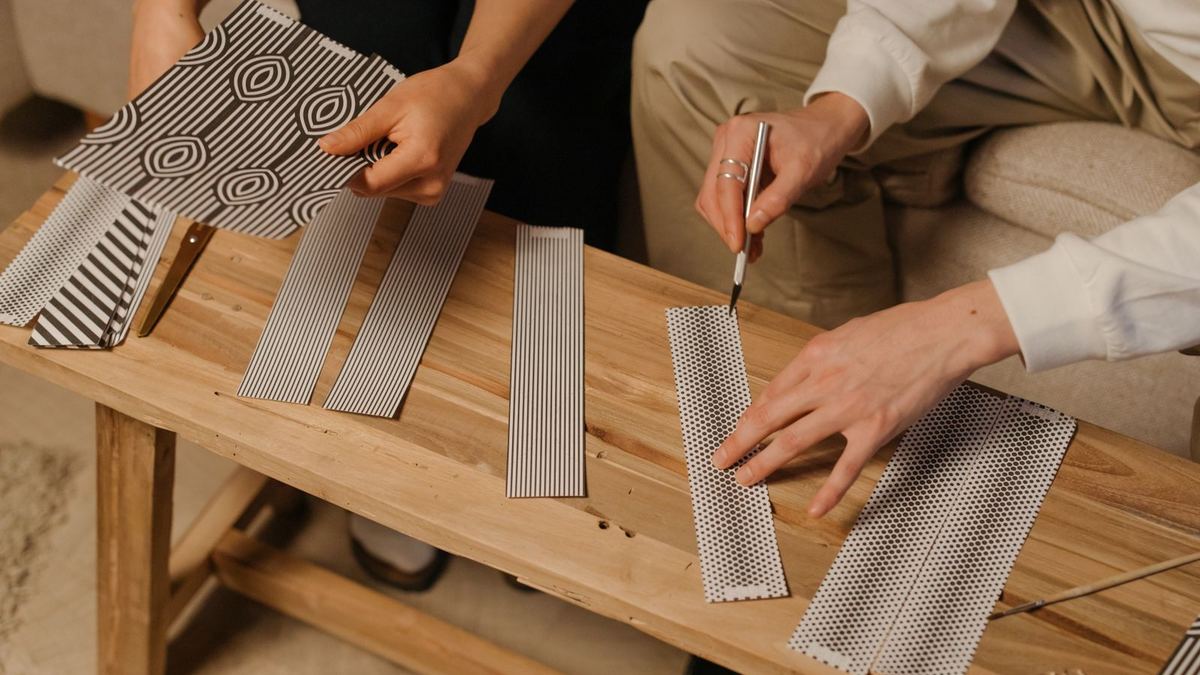 Duas pessoas fazendo artesanato com papel estampado em uma mesa de madeira
