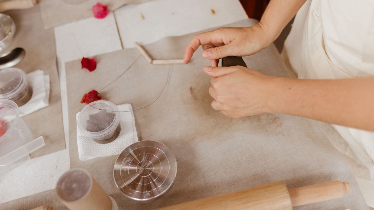 Mãos trabalhando com ferramentas e materiais de artesanato sobre uma mesa