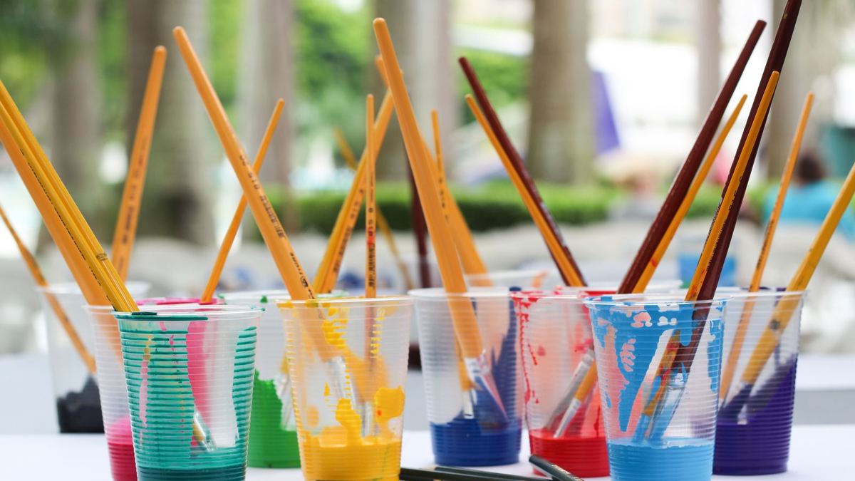 Pincéis e lápis coloridos guardados em copos plásticos