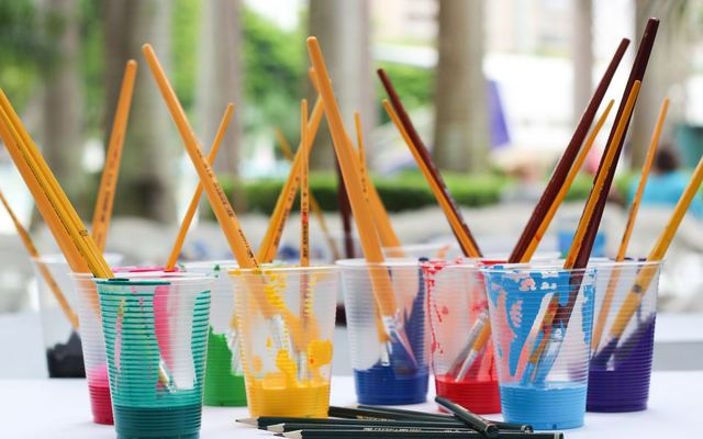Pincéis e lápis coloridos guardados em copos plásticos