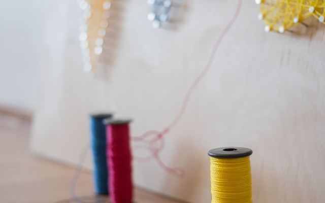 Quadro de string art com pregos e linhas coloridas sobre tábua de madeira