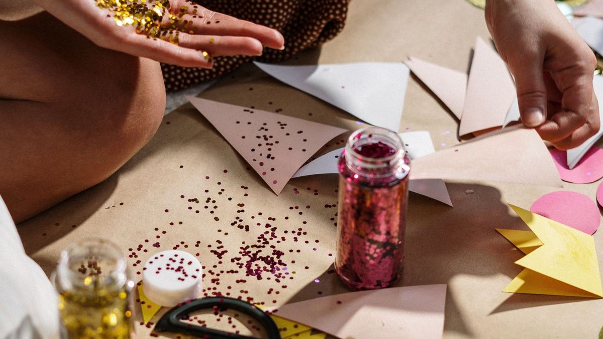 Mãos manuseando papel colorido, fitas e materiais de artesanato