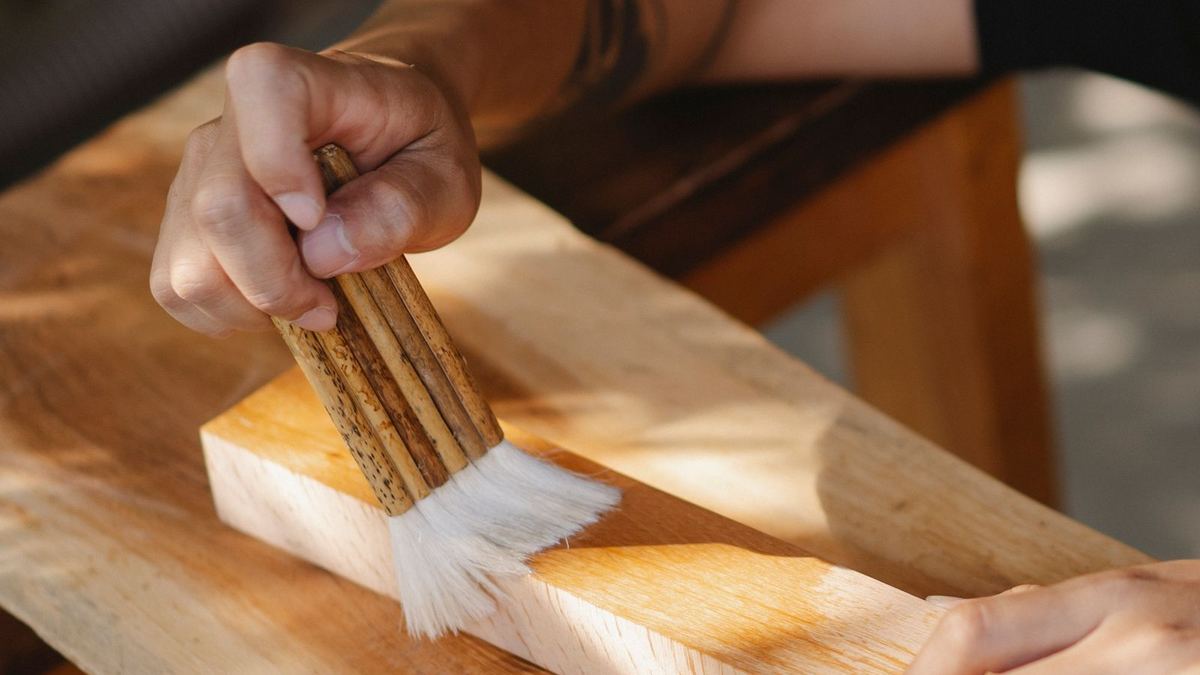Artesão aplicando verniz em uma peça de madeira com pincel