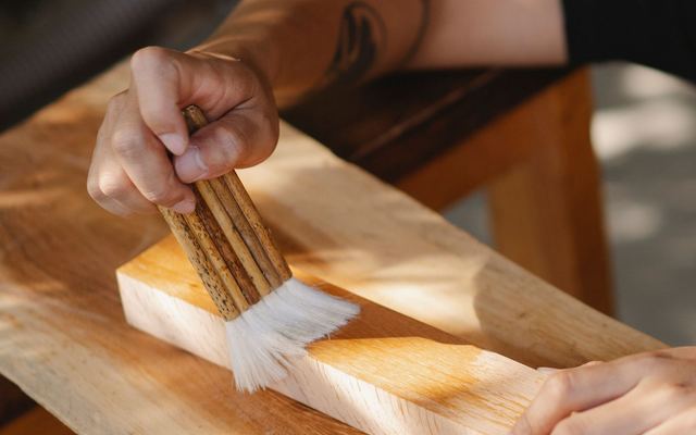 Artesão aplicando verniz em uma peça de madeira com pincel